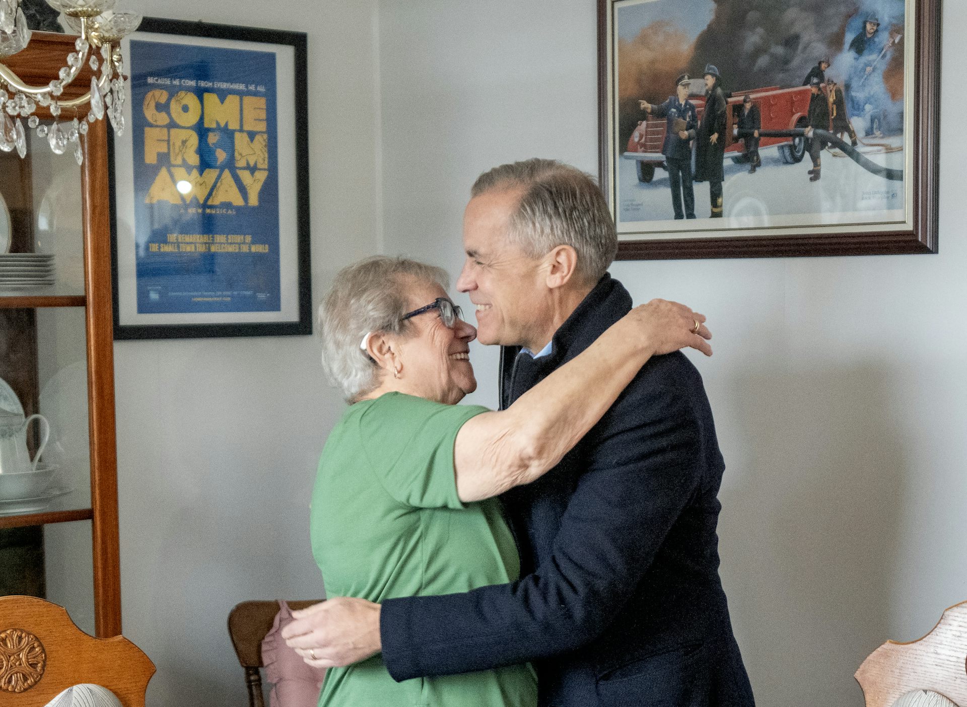An older woman in a green shirt hugs a man with short grey hair.