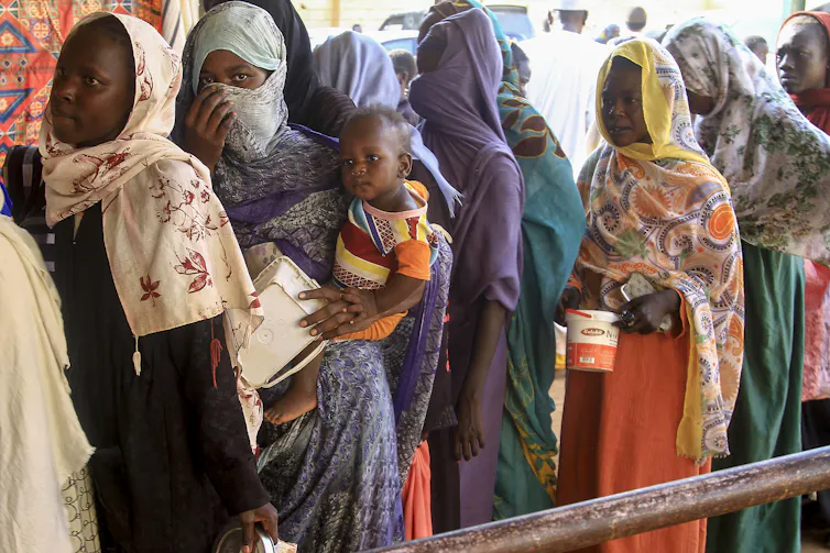 Women and infants line up with some carrying containers