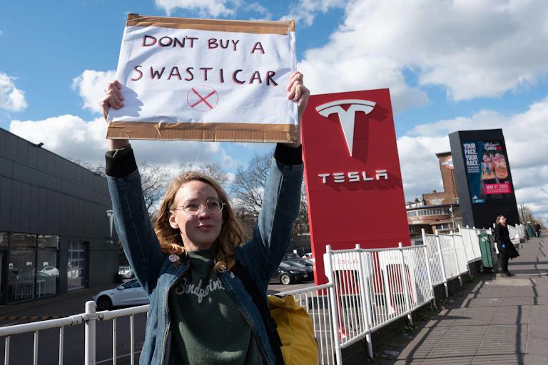 Woman holds up 'don't buy a swasticar' sign outside Tesla dealership