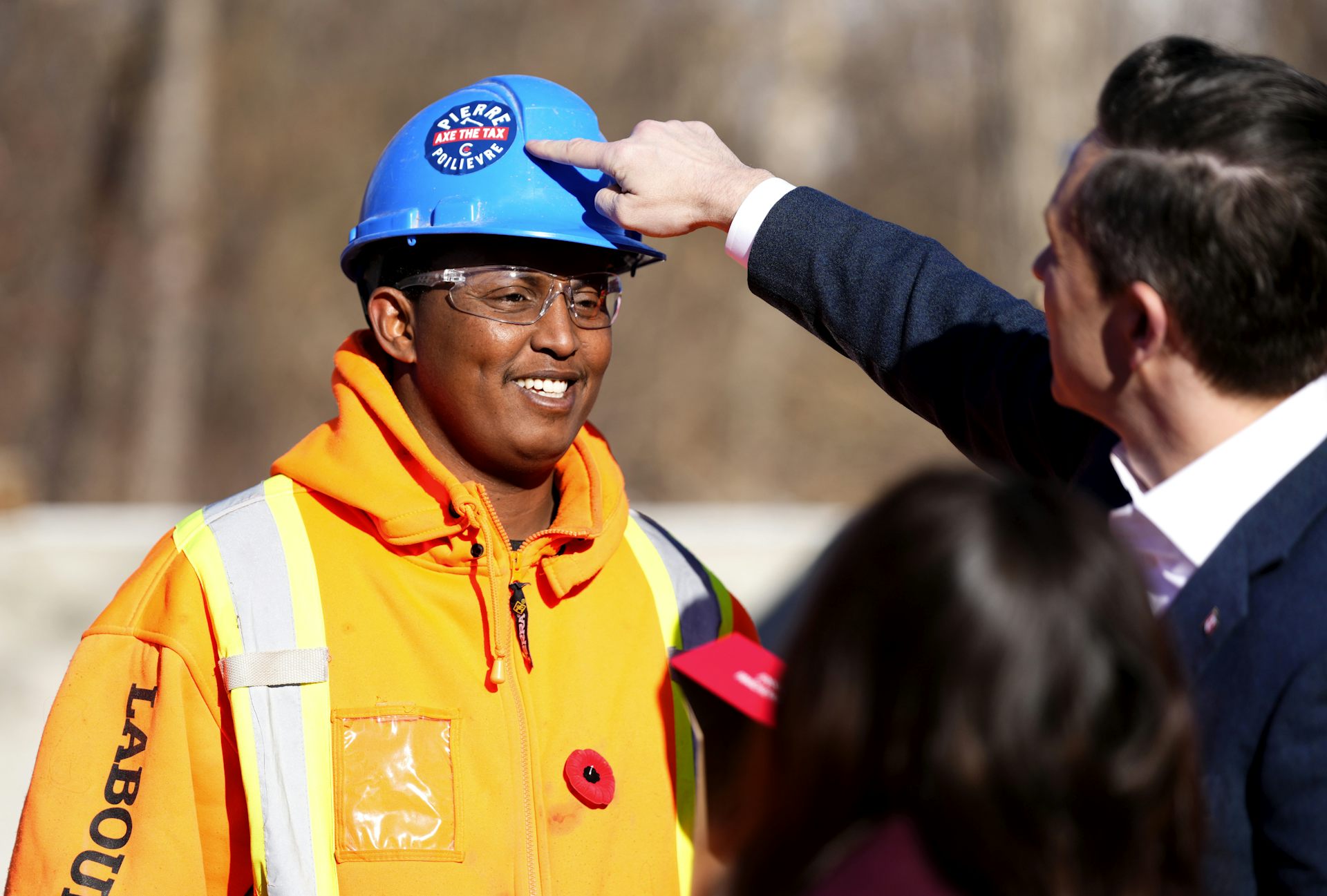 A dark-haired man points to a sticker on a worker's helmet.