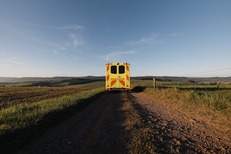 Back view of an ambulance driving down a rural dirt road.