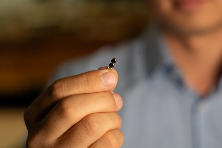 Man's hand holding up a tiny magnet. His face is in the background, out of focus.