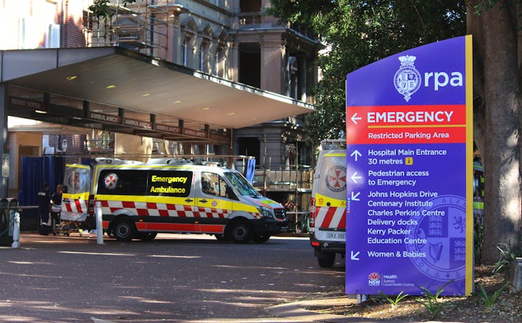 An ambulance parked in font of a hospital and next to a large blue and red sign