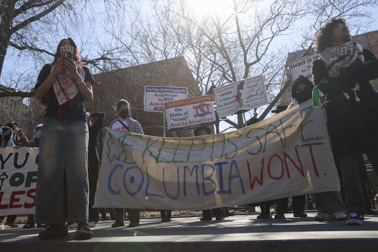 Student activists hold up a banner reading: lWe keep US safe. Columbia won't'.
