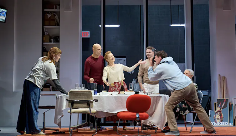 A scene onstage showing a happy family talking and laughing and interacting with one another around a kitchen table.