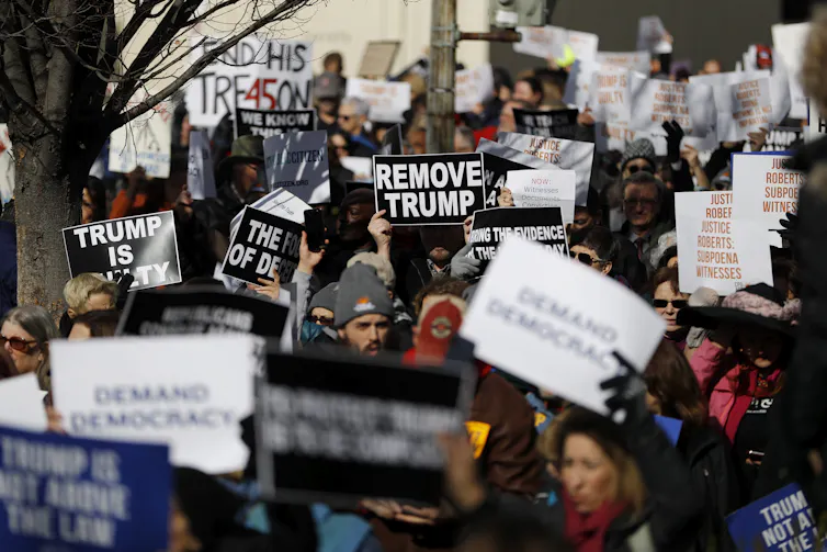A crowd of protesters carry anti-Donald Trump signs. One reads 'Remove Trump'
