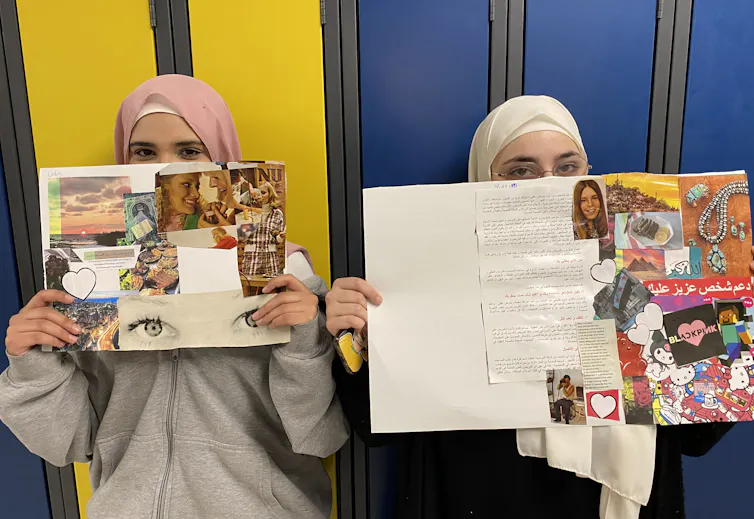 Two girls wearing hijabs hold up collages of their art projects