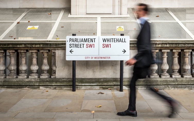 Blurred image of man walking past street signs for Parliament Steet and Whitehall.