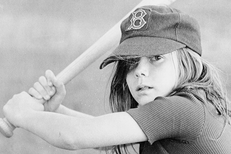 Black and white photo of girl holding a baseball bat and posing in her batting stance.