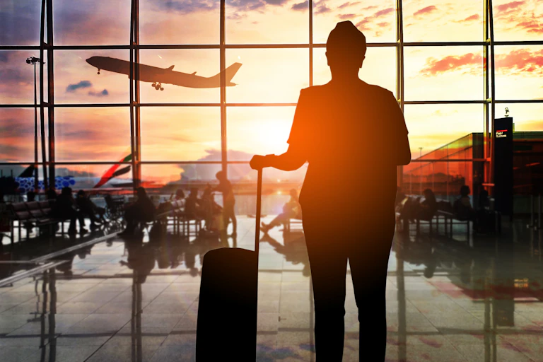 Silhouette of a man with a suitcase watching a plane take off at dusk