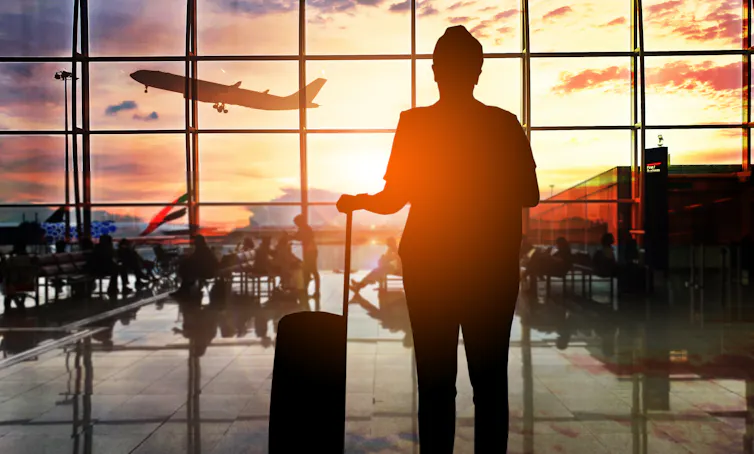Silhouette of a man with a suitcase watching a plane take off at dusk