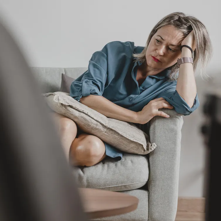 Une femme assise sur une chaise, la tête appuyée sur sa main.
