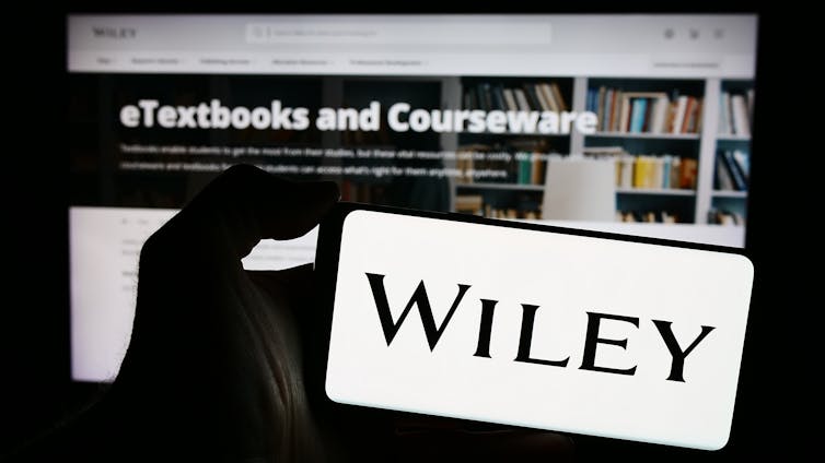 Person holding smartphone with logo of US publishing company John Wiley and Sons Inc. in front of website.