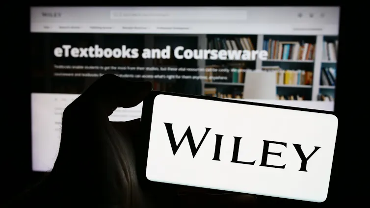 Person holding smartphone with logo of US publishing company John Wiley and Sons Inc. in front of website.