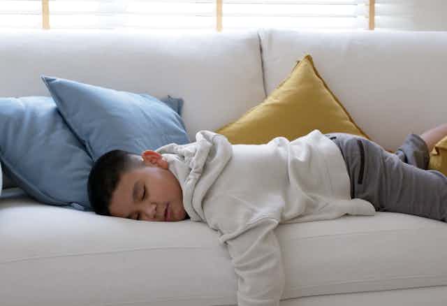 A young boy lies on the couch asleep.