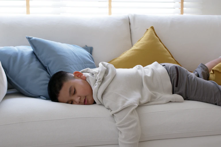 A young boy lies on the couch asleep.
