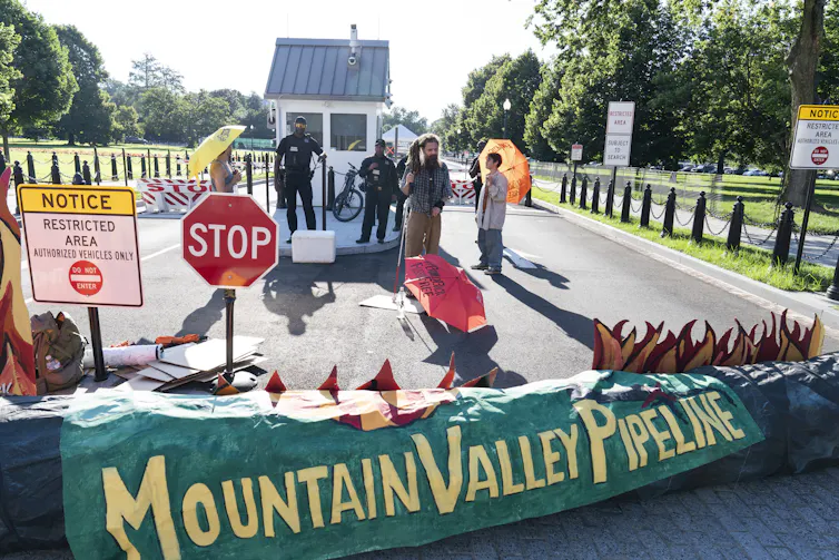 people stand behind a green barrier reading Mountain Valley Pipeline