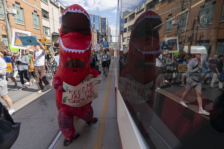 Una persona en los huesos de un dinosaurio rojo caminando por la calle de la ciudad