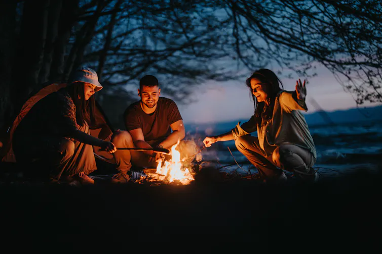 A group of friends sitting around a campfire at night.