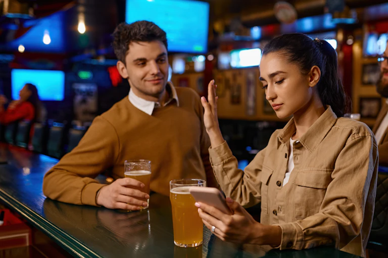 Man approaching woman at a bar, she holds up her hand to show that she's not interested