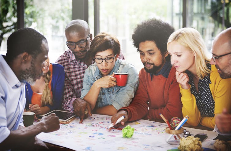 team of people sat around table discussing an idea, drinking coffee