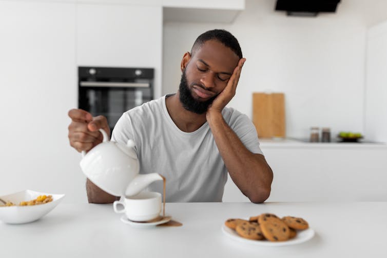 Man sitting at breakfast table pouring tea into an overflowing cup