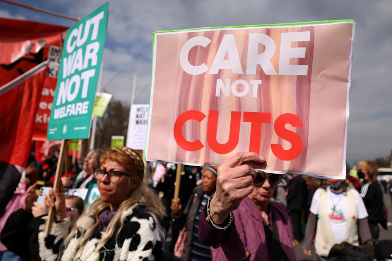 demonstrators protesting against cuts to welfare spending holding signs saying 'care not cuts'
