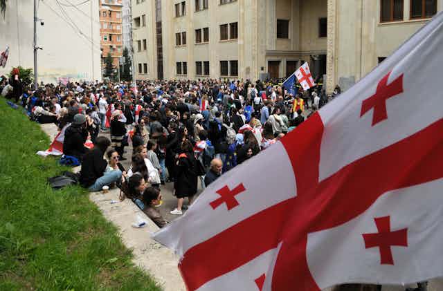 A large red and white flag is seen in front of a crowd of people.