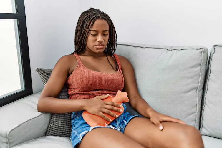 A woman sitting on a sofa holding a hot water bottle to her stomach.