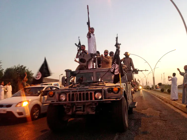 Heavily armed IS fighters in an Iraqi army jeep waving their weapons and IS flags.