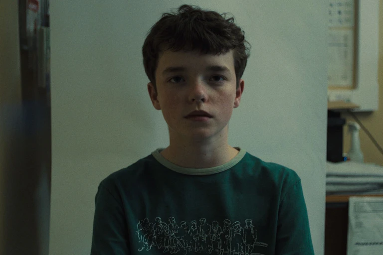 A young boy wearing a t-shirt looks at the camera.