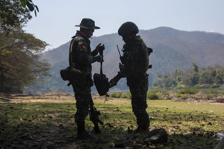 Two men in army fatigues meet amid a backdrop of a mountain.
