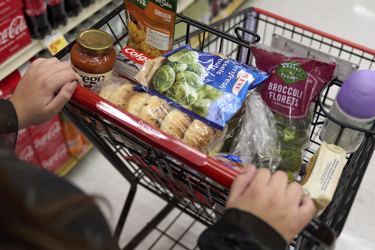 A shopper at a grocery store with food in a cart.