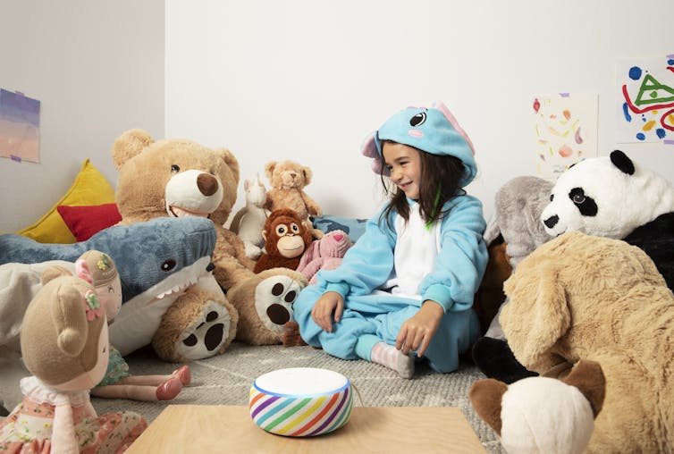 Child setting surrounded by soft toys with a colourful Echo Dot smart speaker.