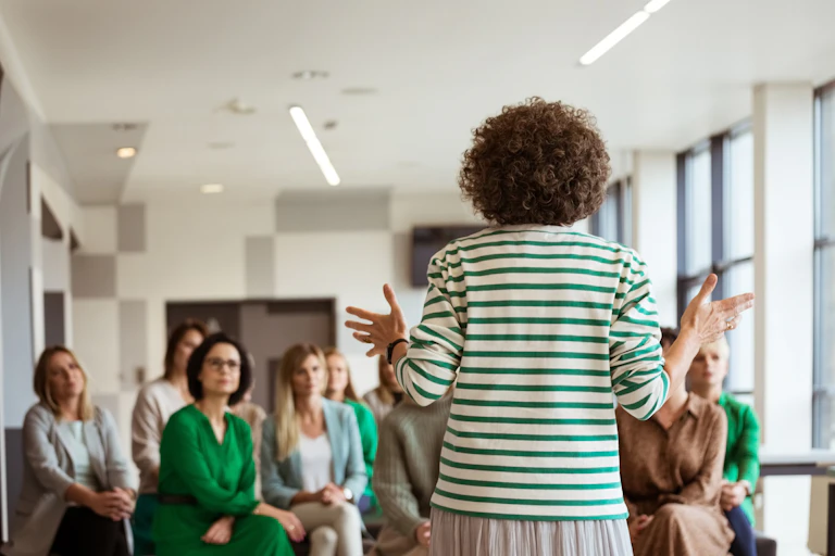 A woman stands and presents to a group of adults sitting down.