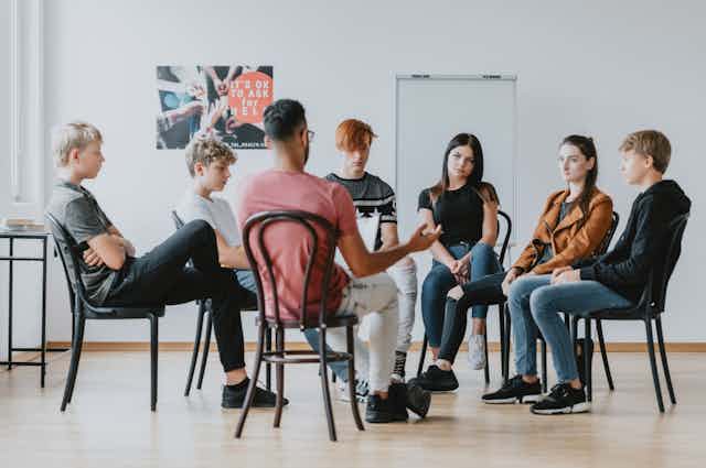 Group of teenagers sitting on chairs in a circle with a therapist or teacher leading discussion