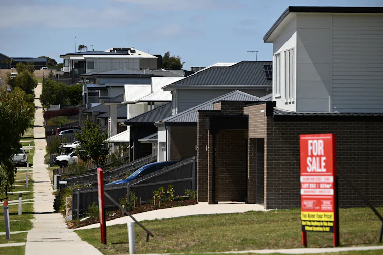 A red for sale sign next to a row of houses stretching into the distanc