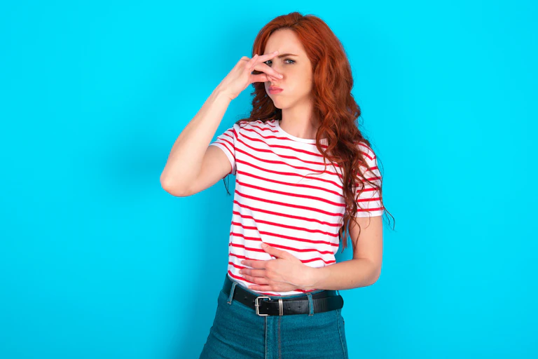 A woman plugs her nose with one hand while pressing a hand onto her stomach with the other hand..