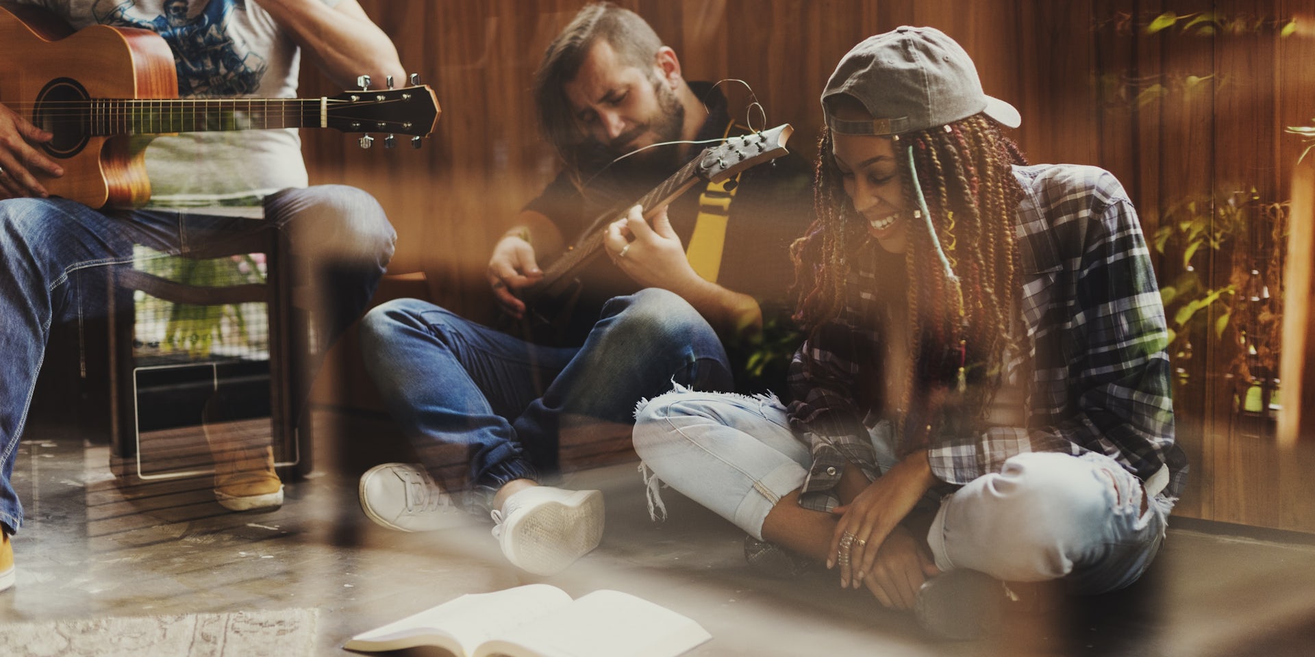 Un chico toca la guitarra mientras una chica a su lado sonríe y mira hacia un libro.