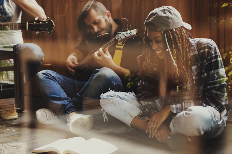 Un chico toca la guitarra mientras una chica a su lado sonríe y mira hacia un libro.