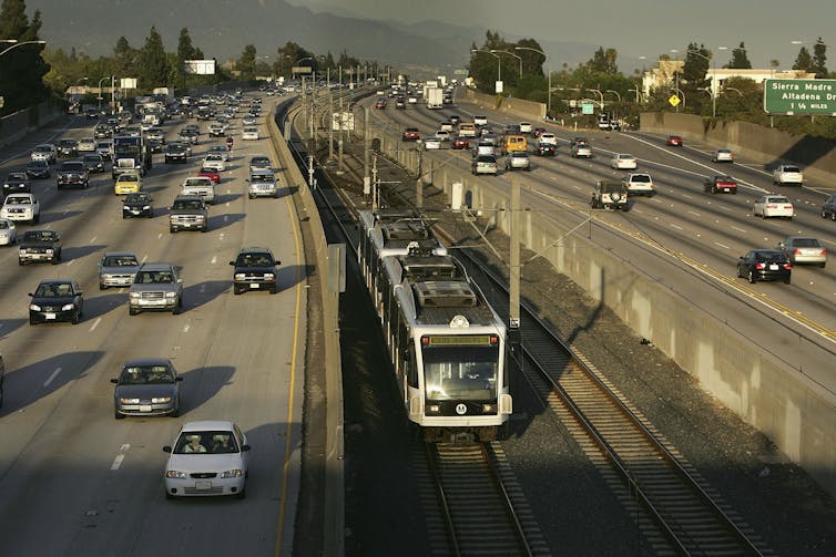 Cars on a 12-lane highway drive alongside a single metro train line.