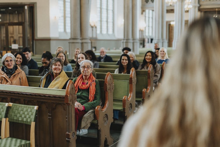 Believers sit in pews as they listen to a priest delivering a sermon in church.