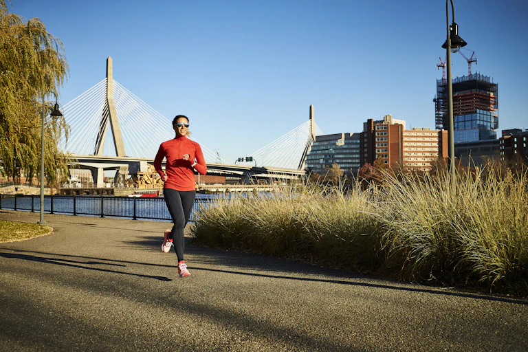 A woman runs beside a river with a city in the background