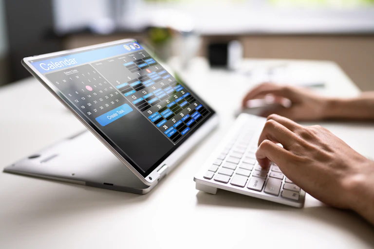 woman's hand typing on a keyboard with a screen showing an online calendar