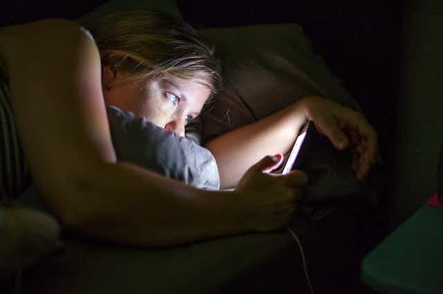 Side view of a woman staring at her phone in the dark.