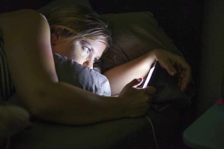 Side view of a woman staring at her phone in the dark.