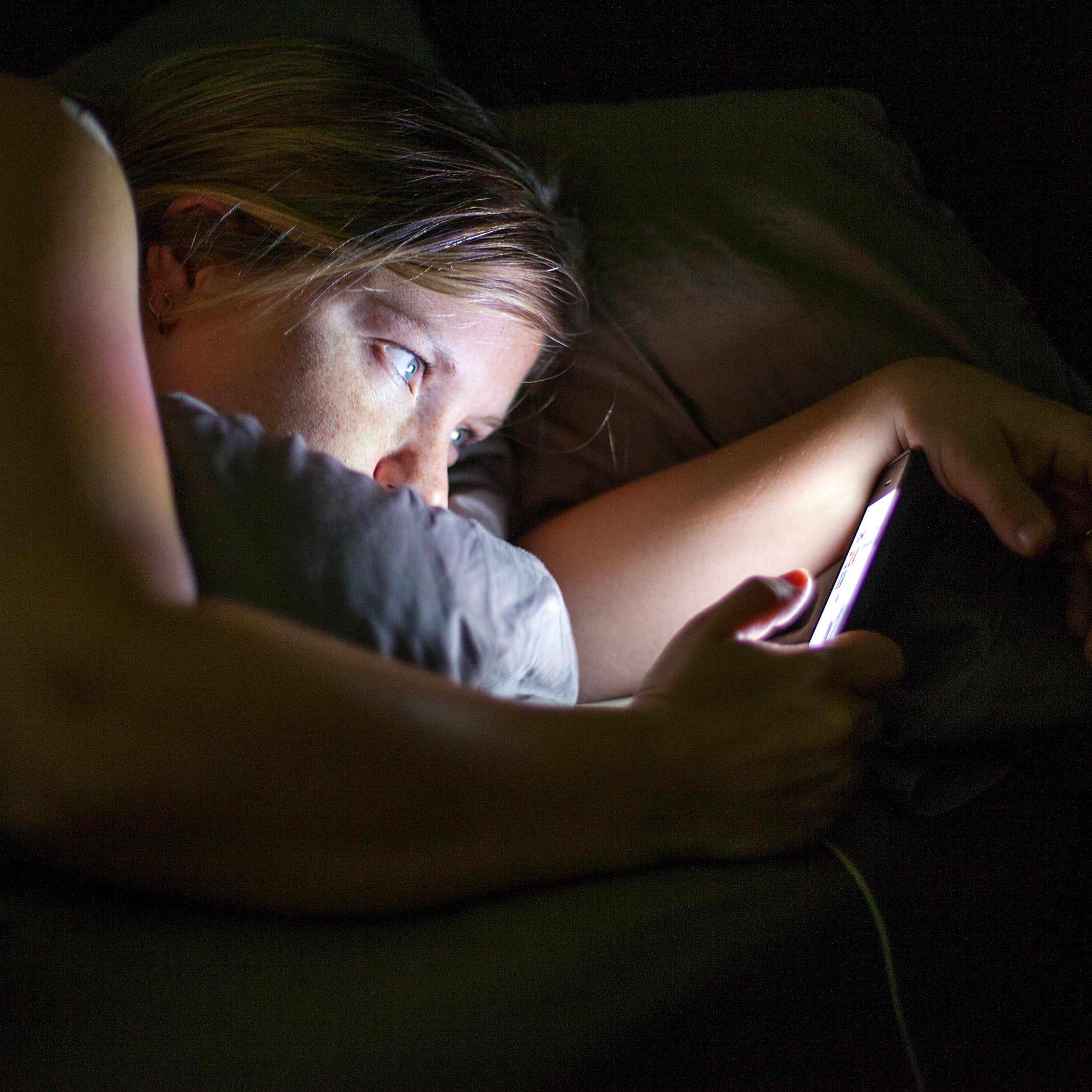 Side view of a woman staring at her phone in the dark.