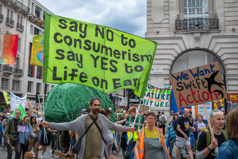 anti-consumerism protesters holding signs and marching in a London street.