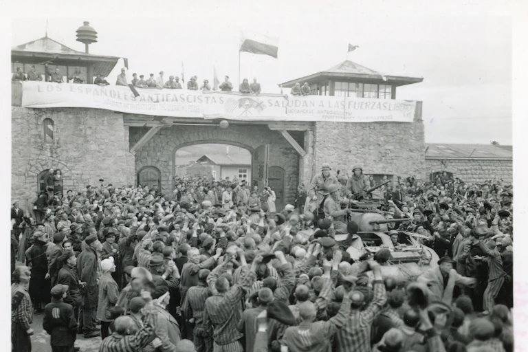 A crowd cheers the arrival of US troops to a concentration camp. Black and white shot.