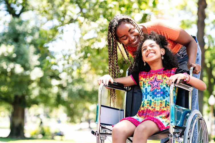 A woman and young girl in a wheelchair in a park